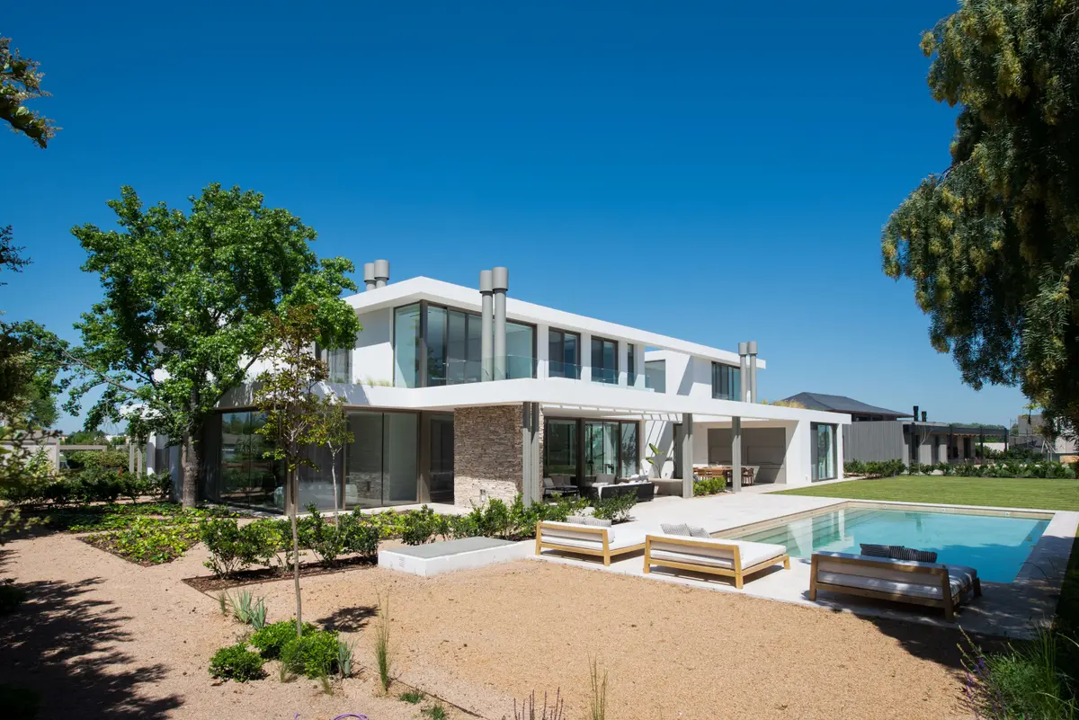 Casa moderna con piscina y jardín exuberante, fachada blanca — proyecto Casa AA, por Estudio Junor, en Pilar